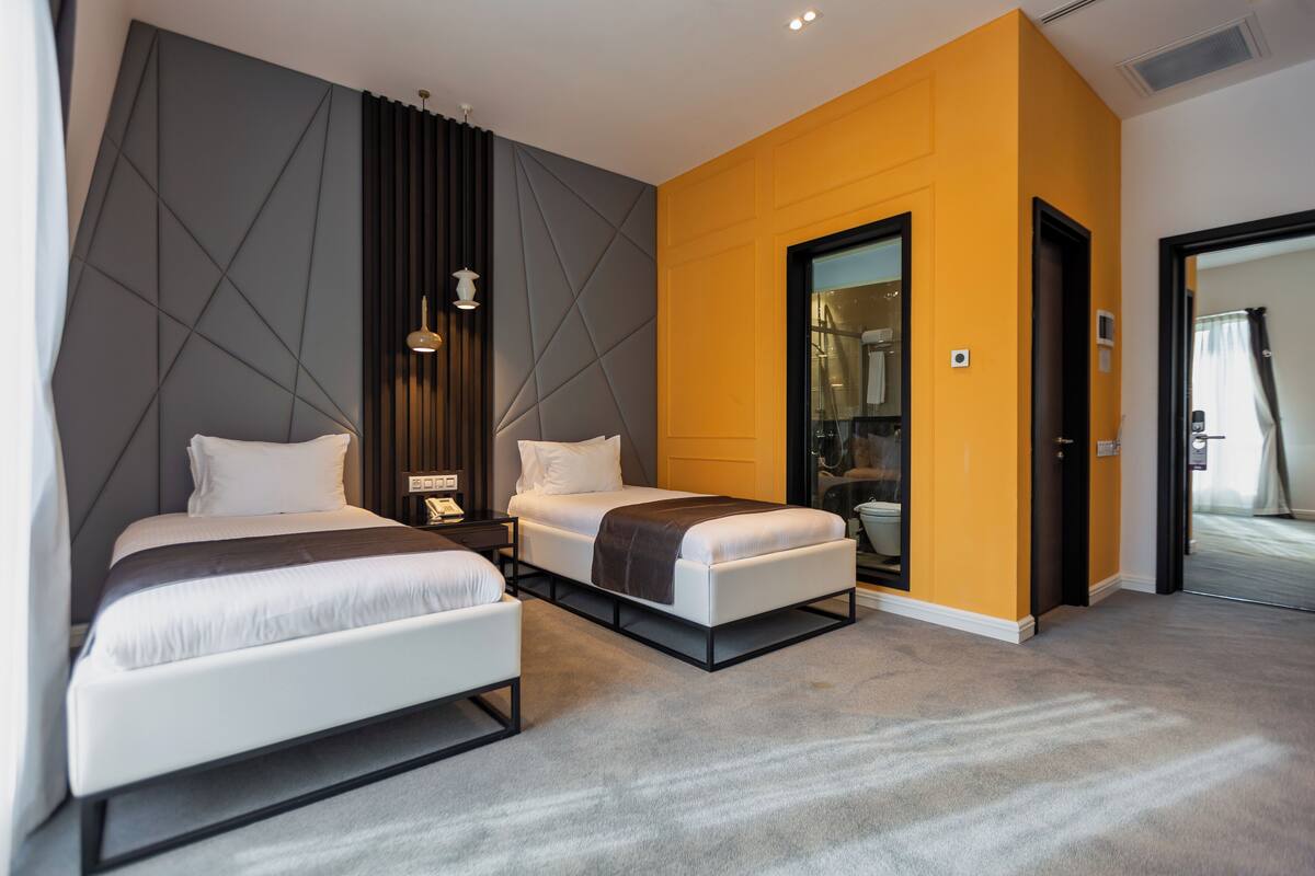 A modern hotel room with two beds, a large mirror, and a wardrobe.