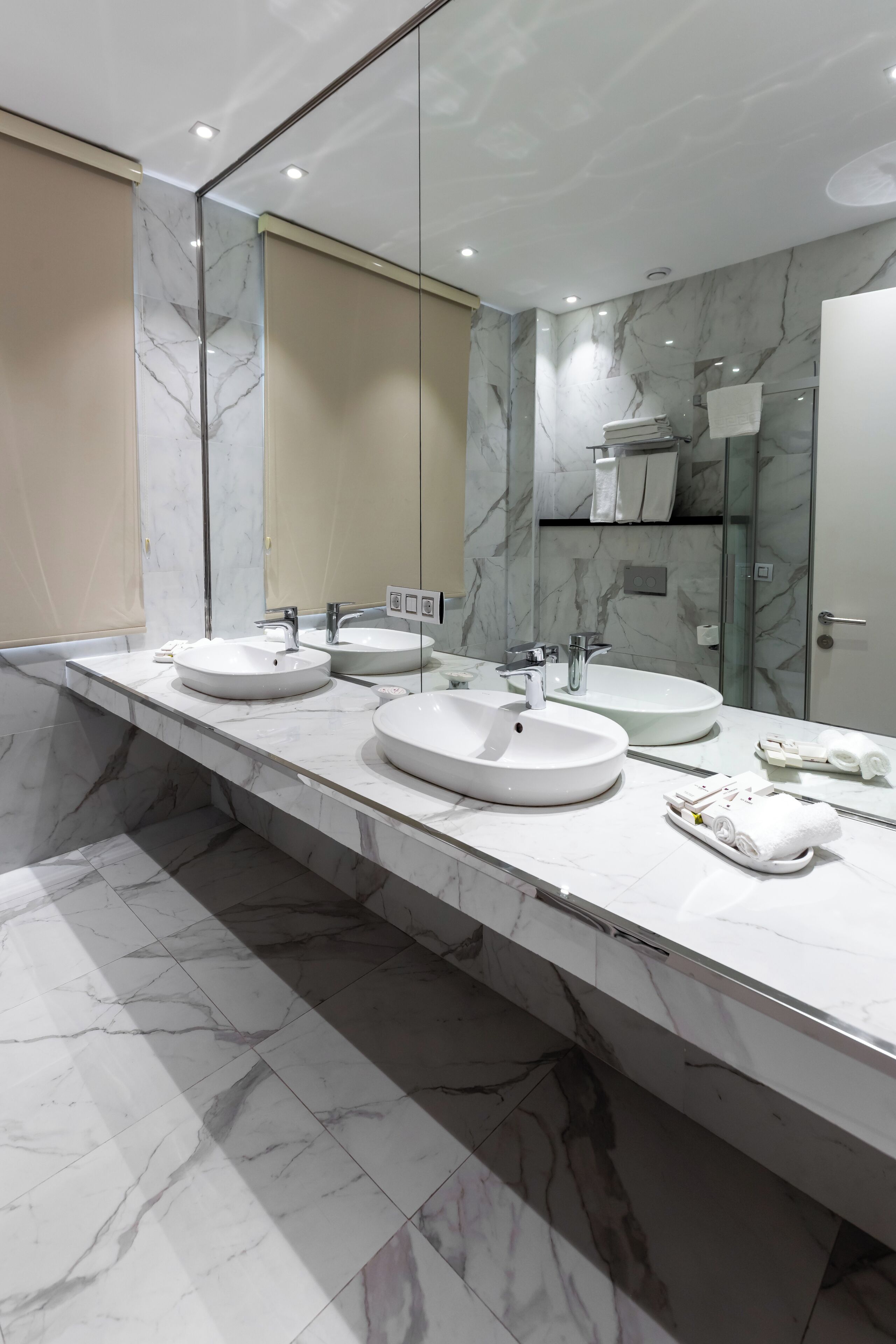 A modern bathroom with two sinks, a large mirror, and marble flooring.
