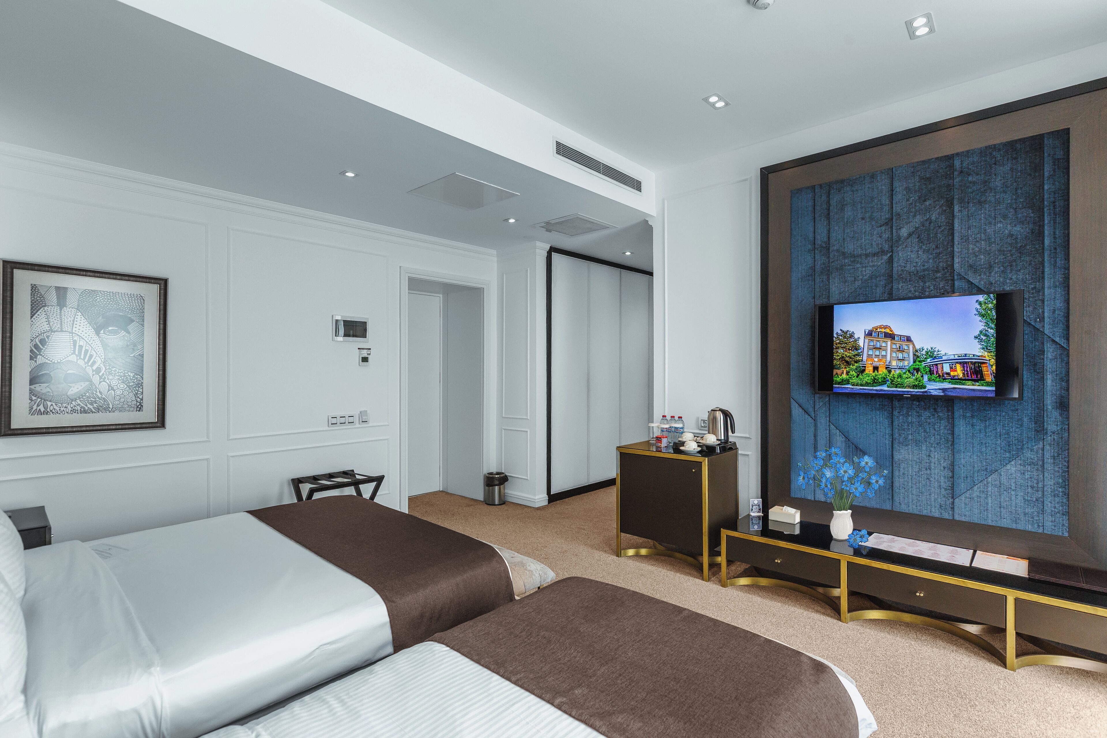 A hotel room with two beds, a TV mounted on a textured wall, a small side table, and a door leading to another room.
