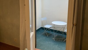 A small outdoor area with a white table and a folding chair, a door leading to a balcony, and a tiled floor.