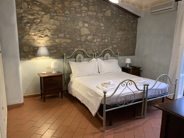 A bedroom with a stone wall, a metal bed frame, a wooden nightstand, and a bedside table with a lamp. - Purgatorio Double in Firenze (Florence)