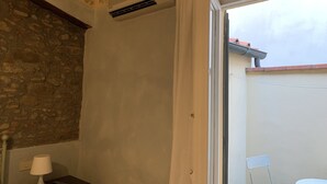 A room with a stone wall, a white lamp, a remote control, a white curtain, a white chair, and a small table.