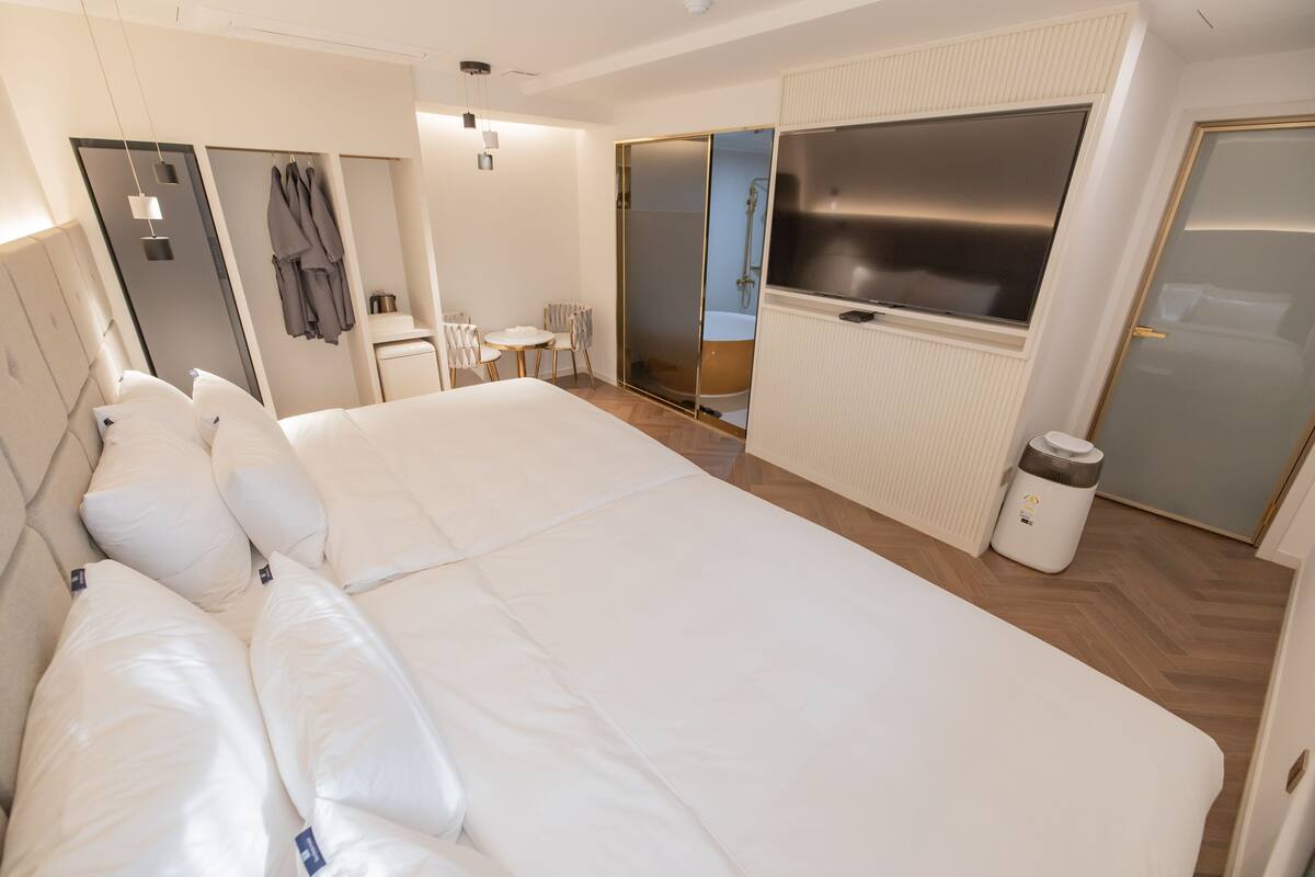 A modern hotel room with a large bed, a shower area, a small seating area, and a TV.