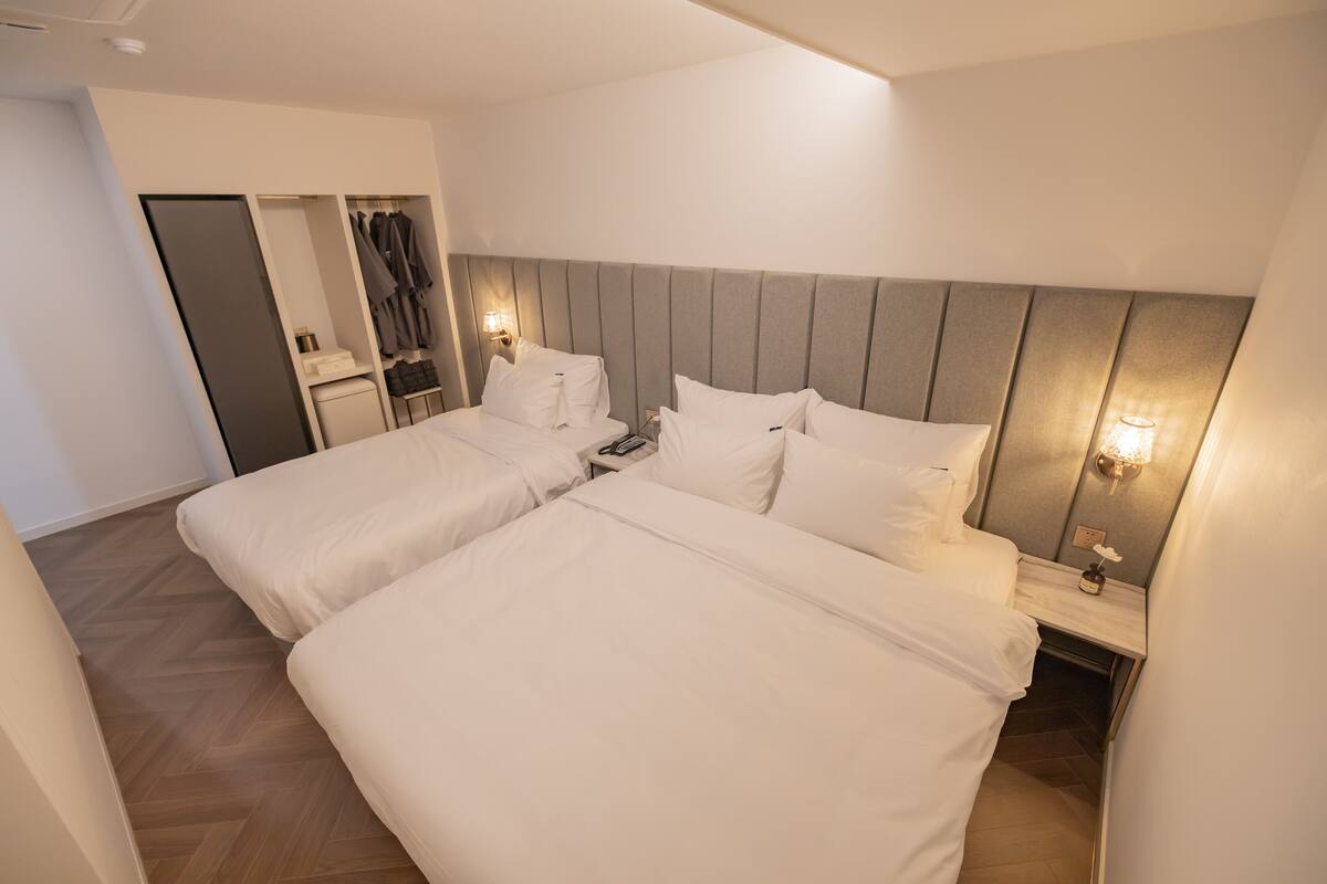 A hotel room with two beds, a wardrobe, a vanity with a mirror, and bedside lamps.