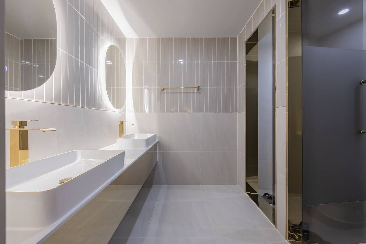 A modern bathroom with three sinks, a large mirror, and a shower area.