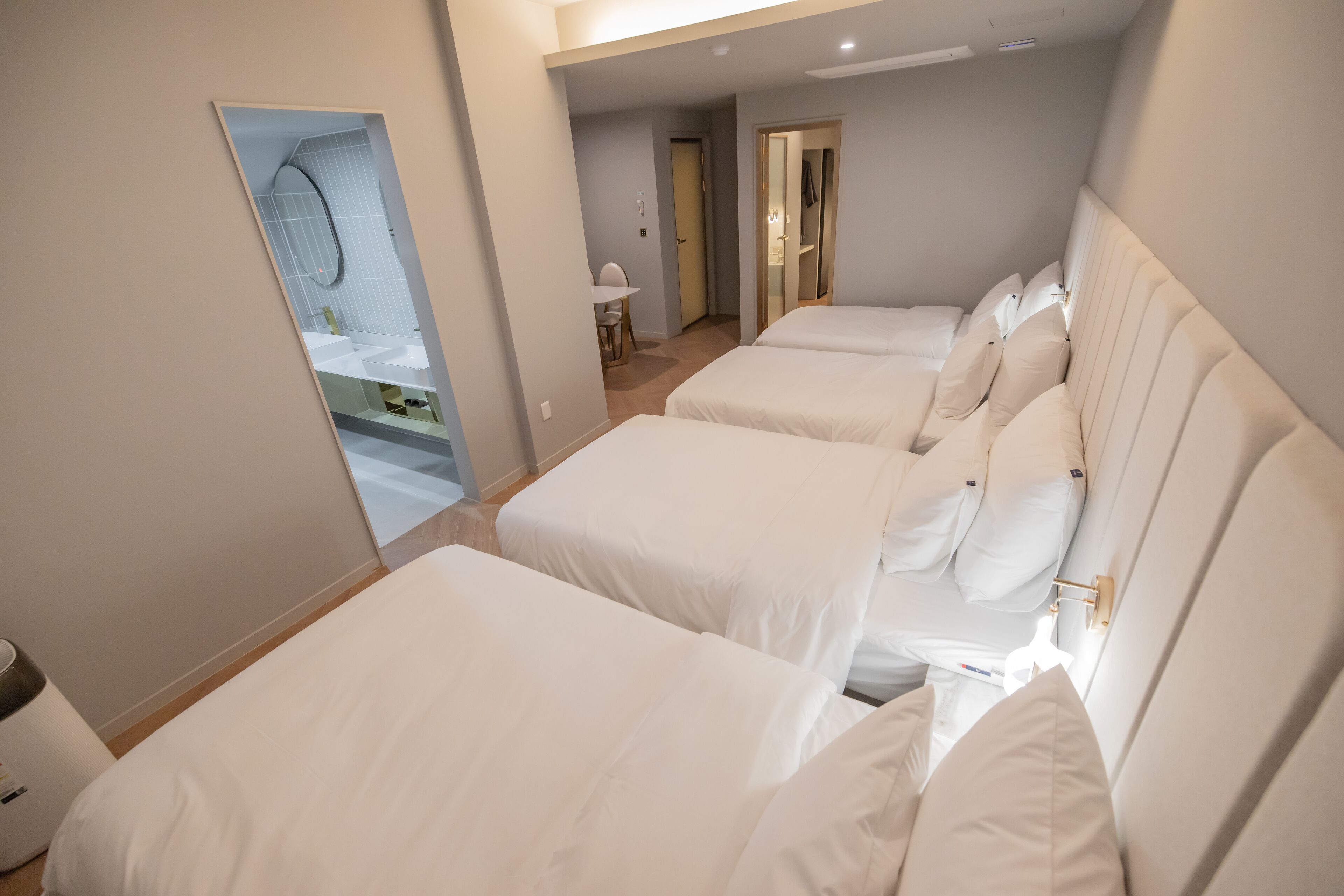 Une chambre d’hôtel avec trois lits, une salle de bain dotée d’un grand miroir et un petit bureau avec une chaise.