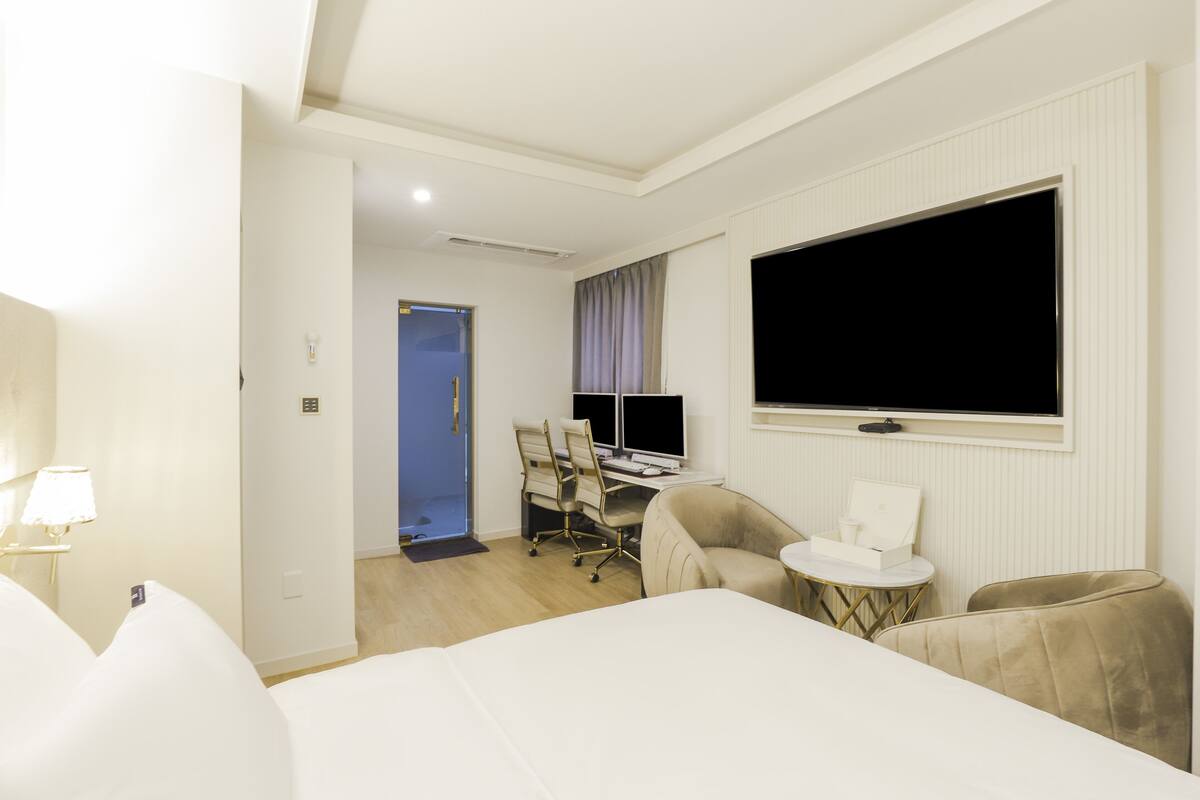 A hotel room with a bed, a desk with a computer, a TV, and a seating area.