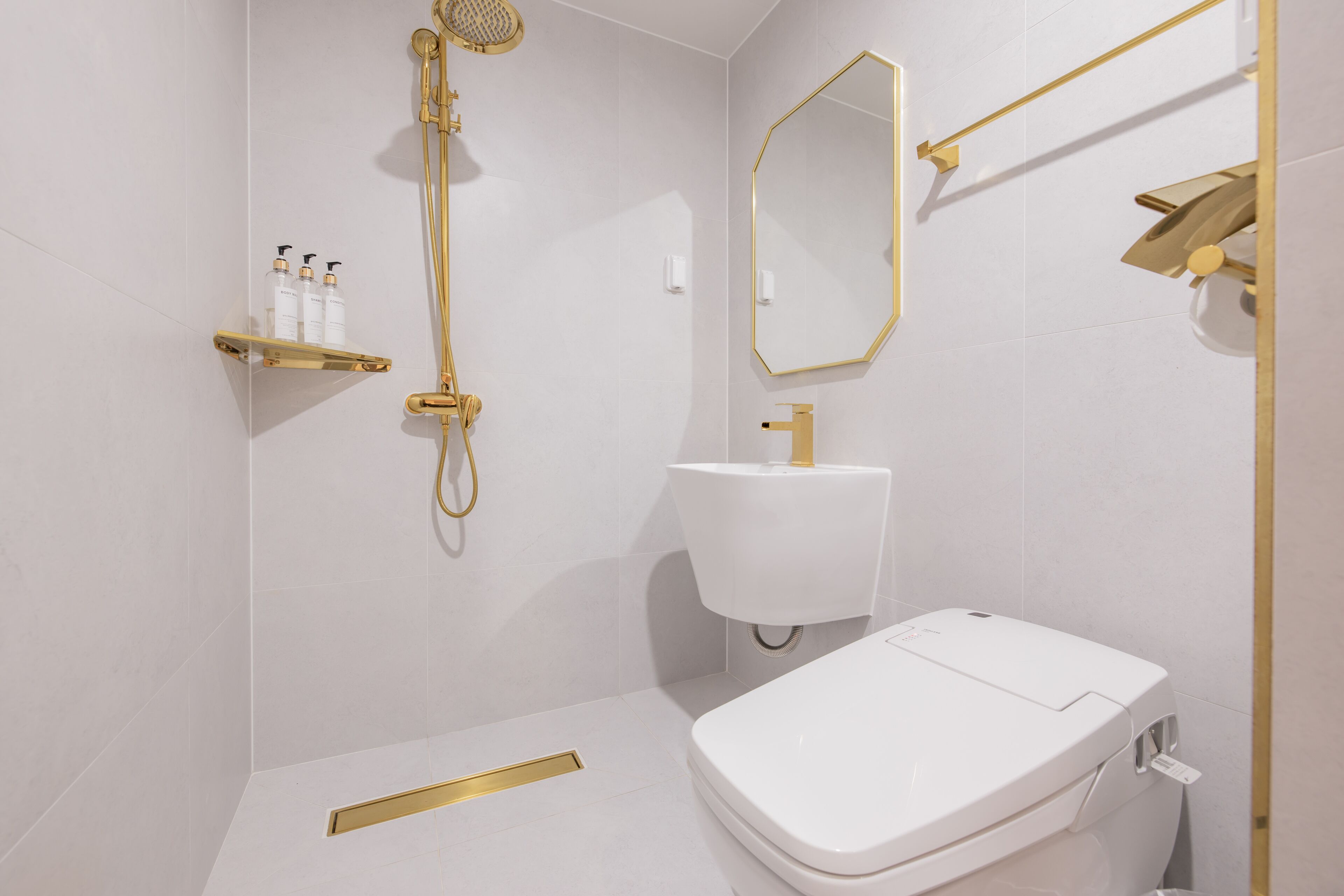 Un baño moderno con inodoro blanco, detalles dorados y ducha.