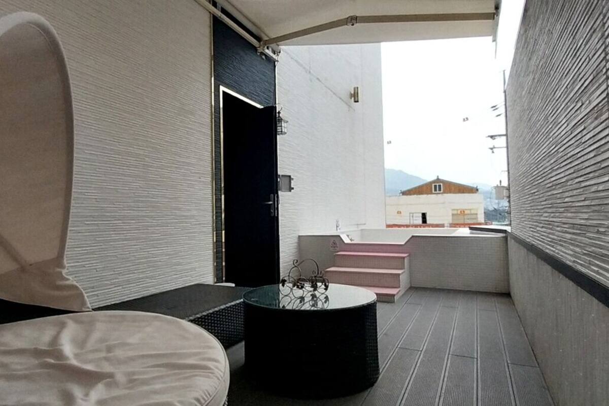 A modern bedroom with a bed, a small table, and a view of a building through an open door.