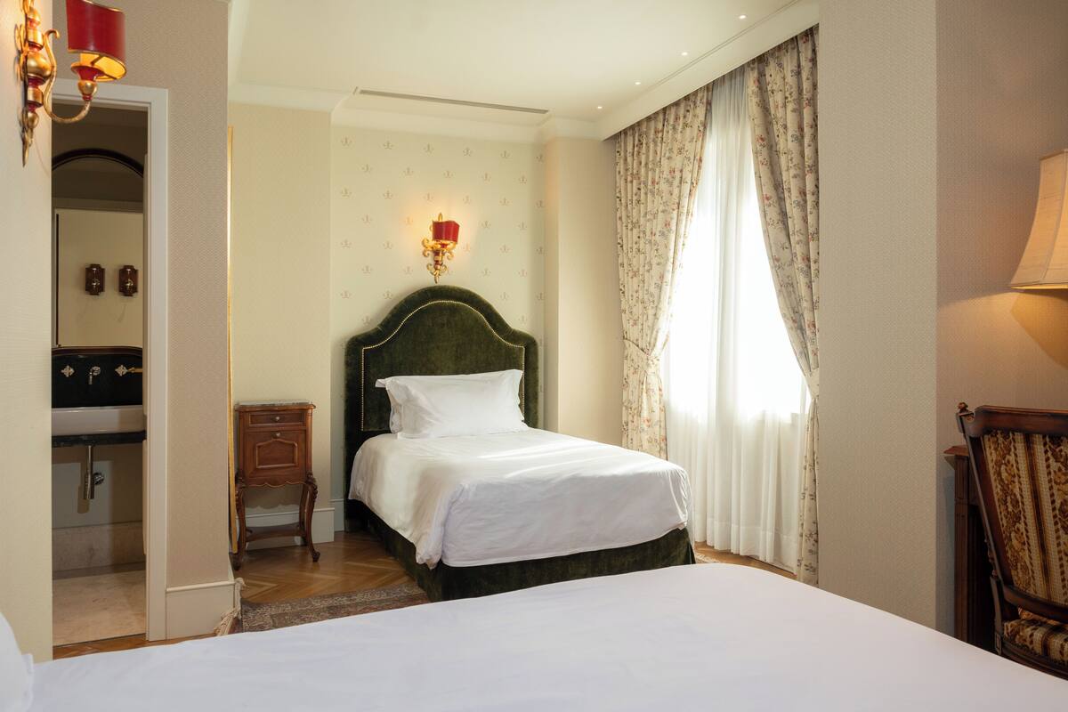 A hotel room with a bed, a nightstand, a mirror, a dresser, and a window with curtains.