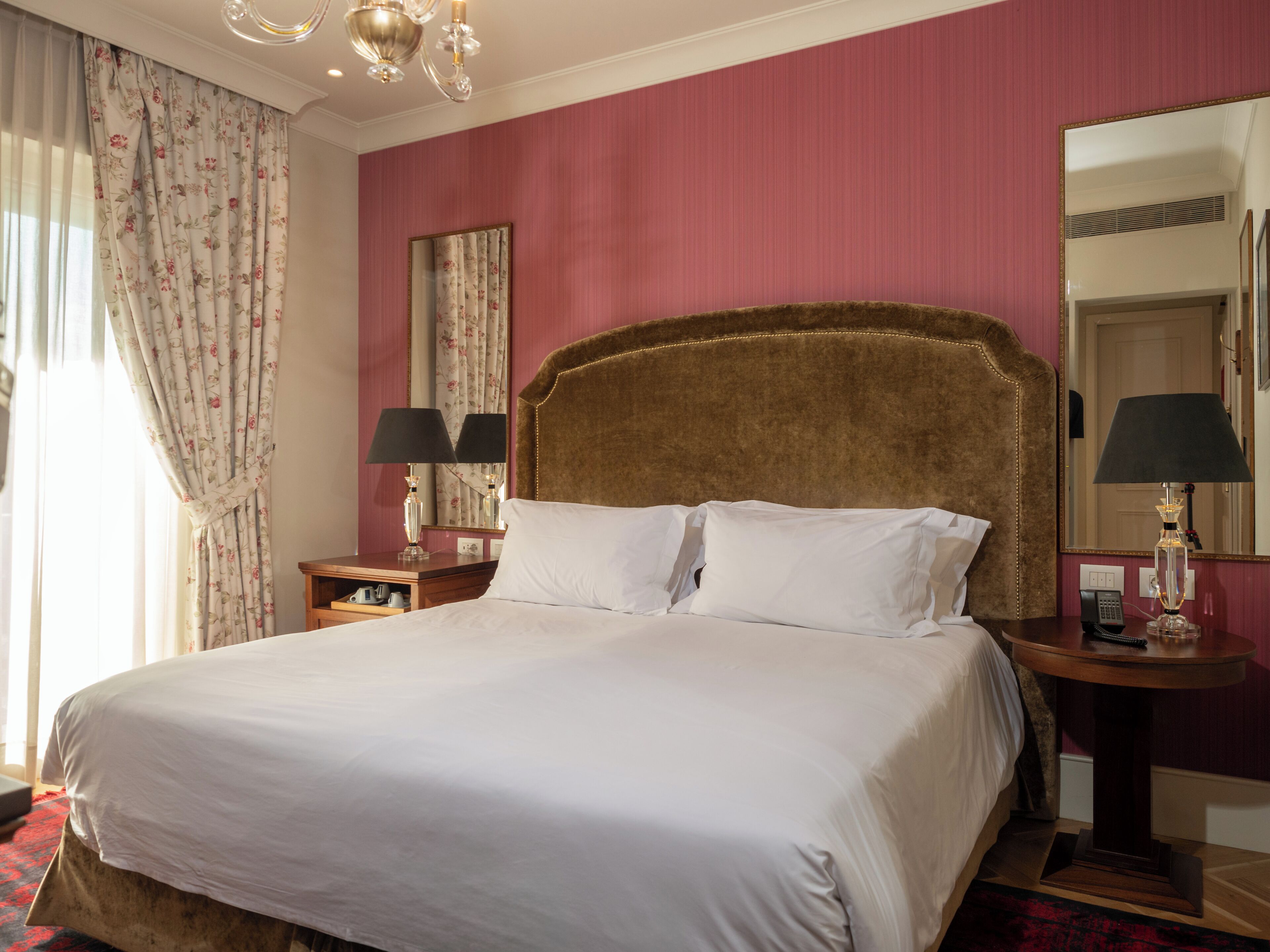 A hotel room with a large bed, two bedside tables with lamps, a mirror, and a red carpet.