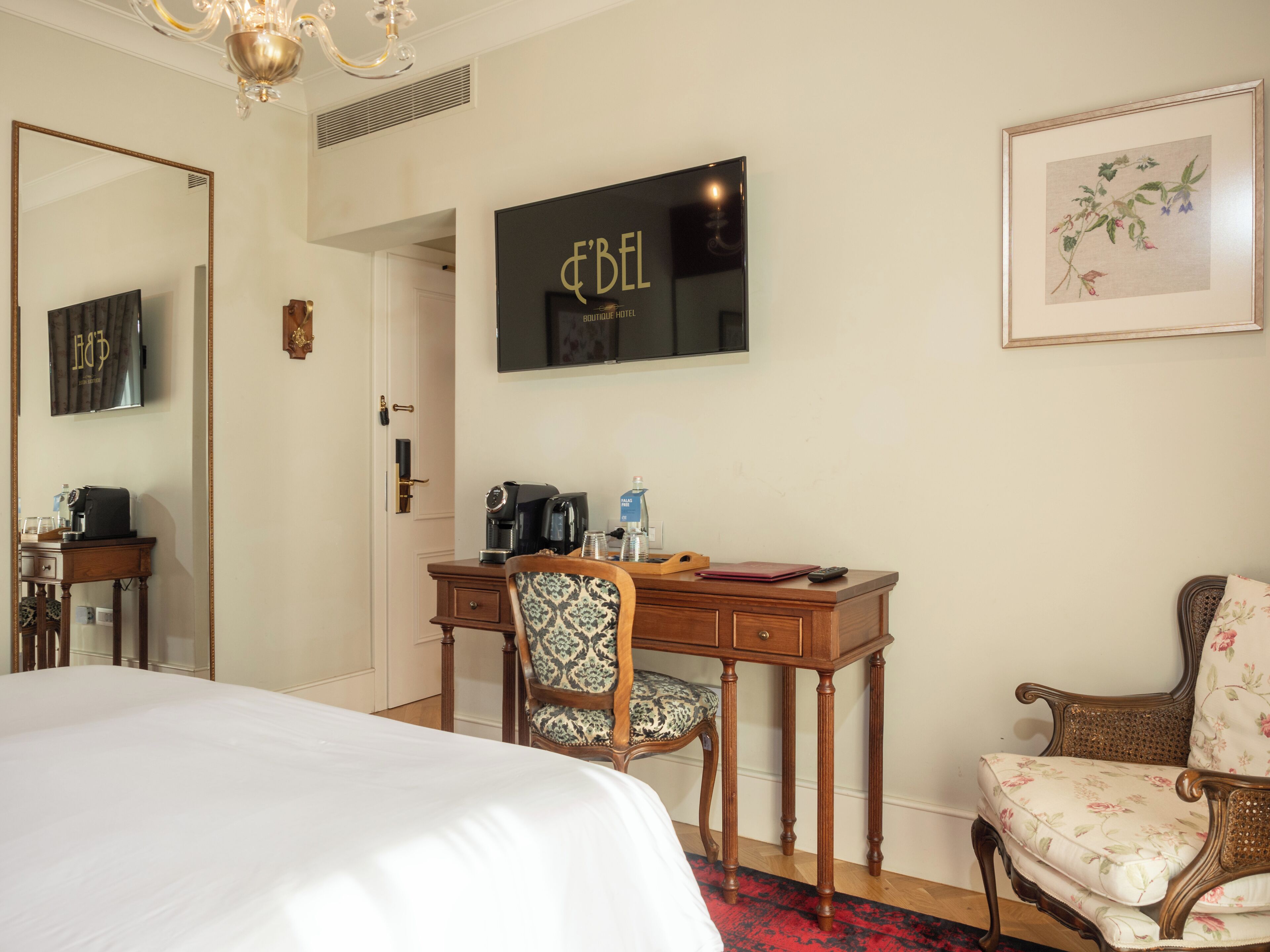 Une chambre d’hôtel comprenant un lit, un bureau avec une machine à café, une chaise, un tableau encadré et un miroir.