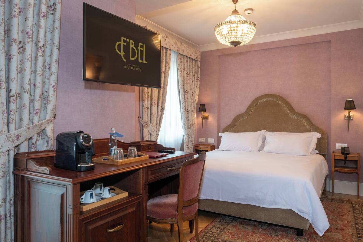 A hotel room with a bed, desk, chair, and a television displaying the hotel's name.