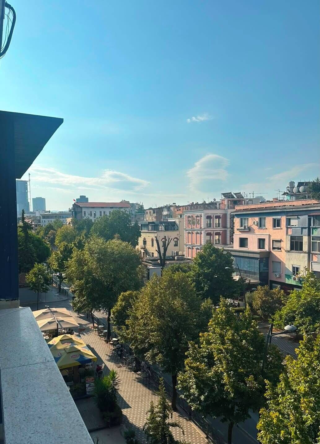 Paisagem urbana com edifícios, árvores e céu claro.