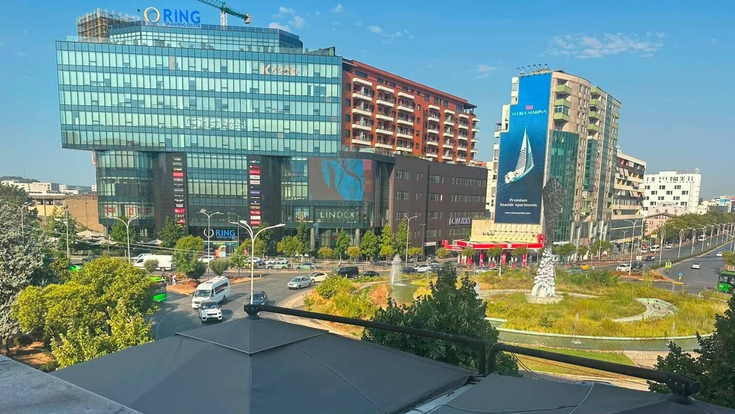 A modern building with a glass facade, a parking lot, and a fountain in the foreground.