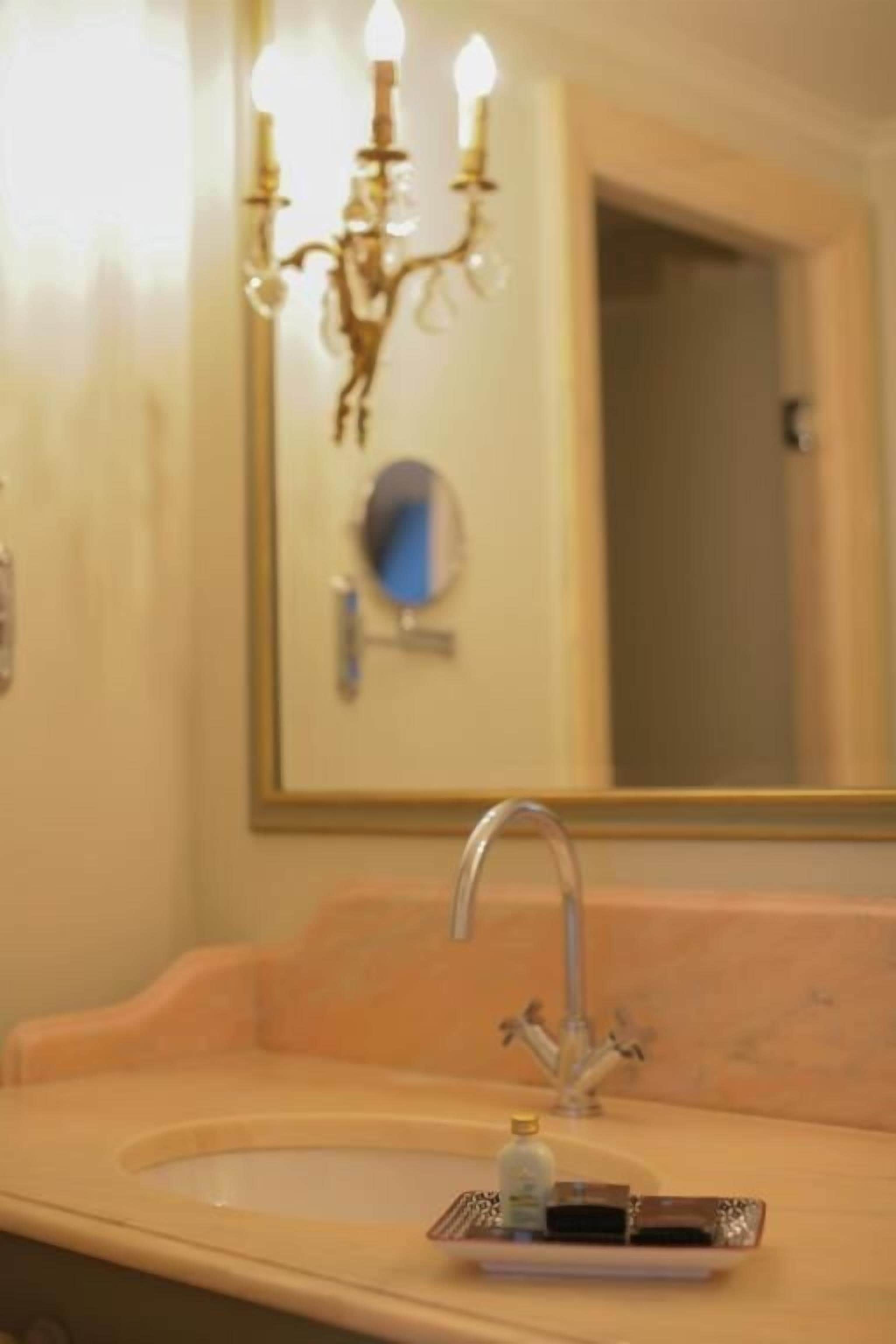 Un baño con lavamanos, espejo y candelabro.