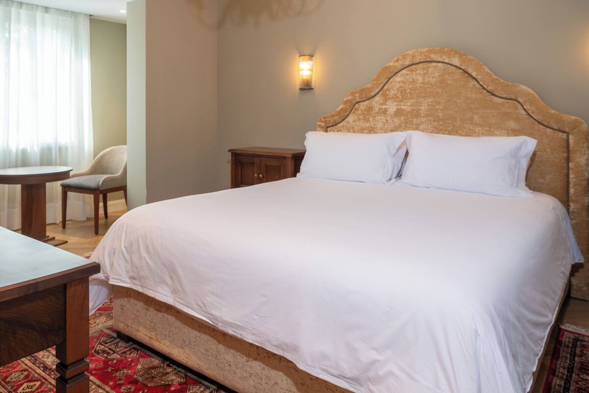 A hotel room with a large bed, a wooden nightstand, a chair, and a small table.
