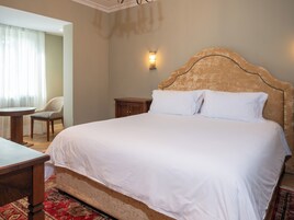 Quarto de hotel com uma cama grande, uma mesa de cabeceira de madeira, uma cadeira e uma pequena mesa.