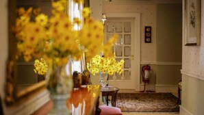 Une pièce avec une table en bois, un vase de fleurs jaunes, une chaise rouge, un tapis à motifs et une porte au fond.