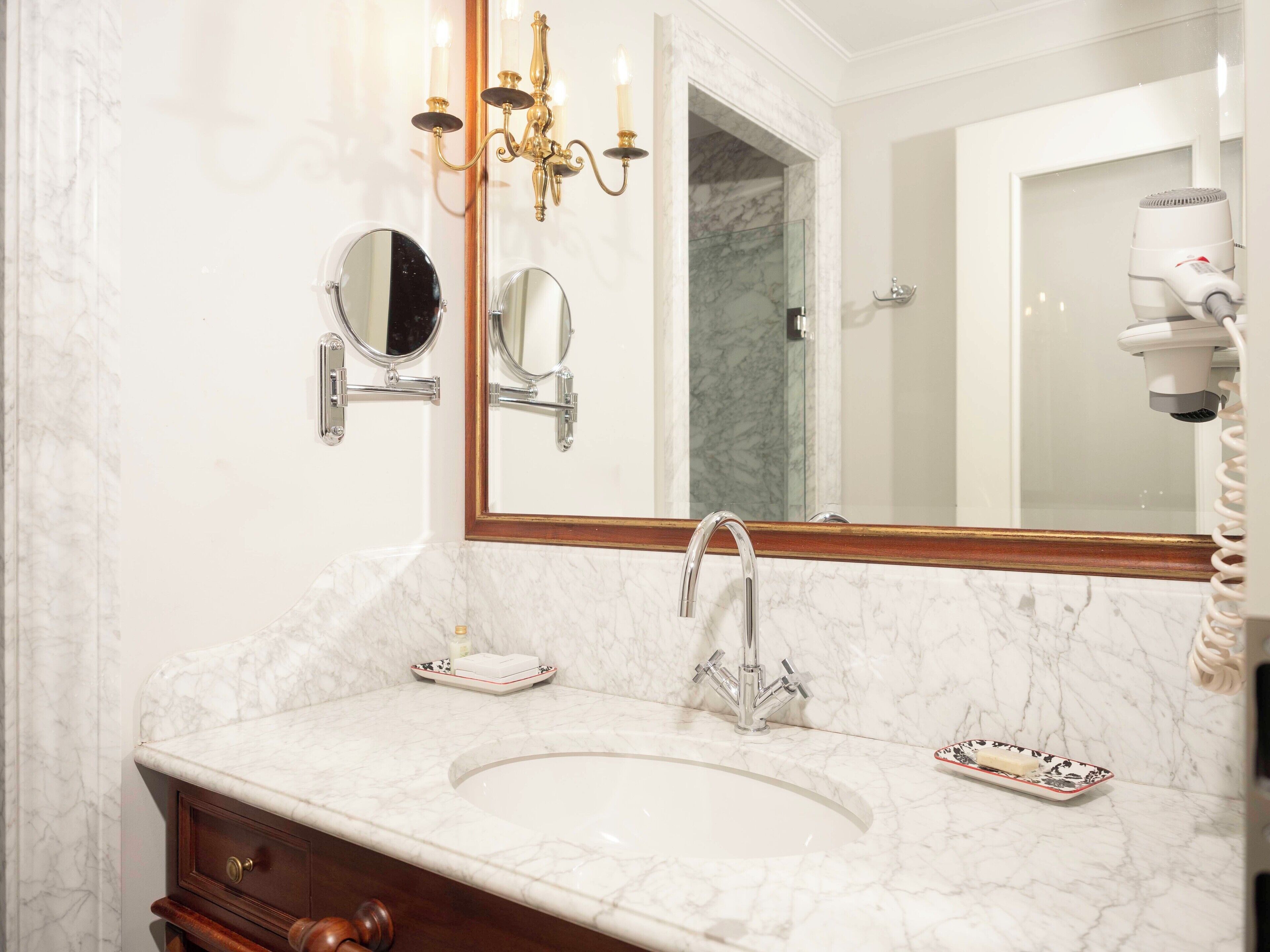 A bathroom with a marble sink, two mirrors, a chandelier, and a hairdryer.