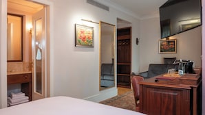 Une chambre d’hôtel comprenant un lit, un bureau avec une chaise, une armoire, un miroir et un tableau accroché au mur.