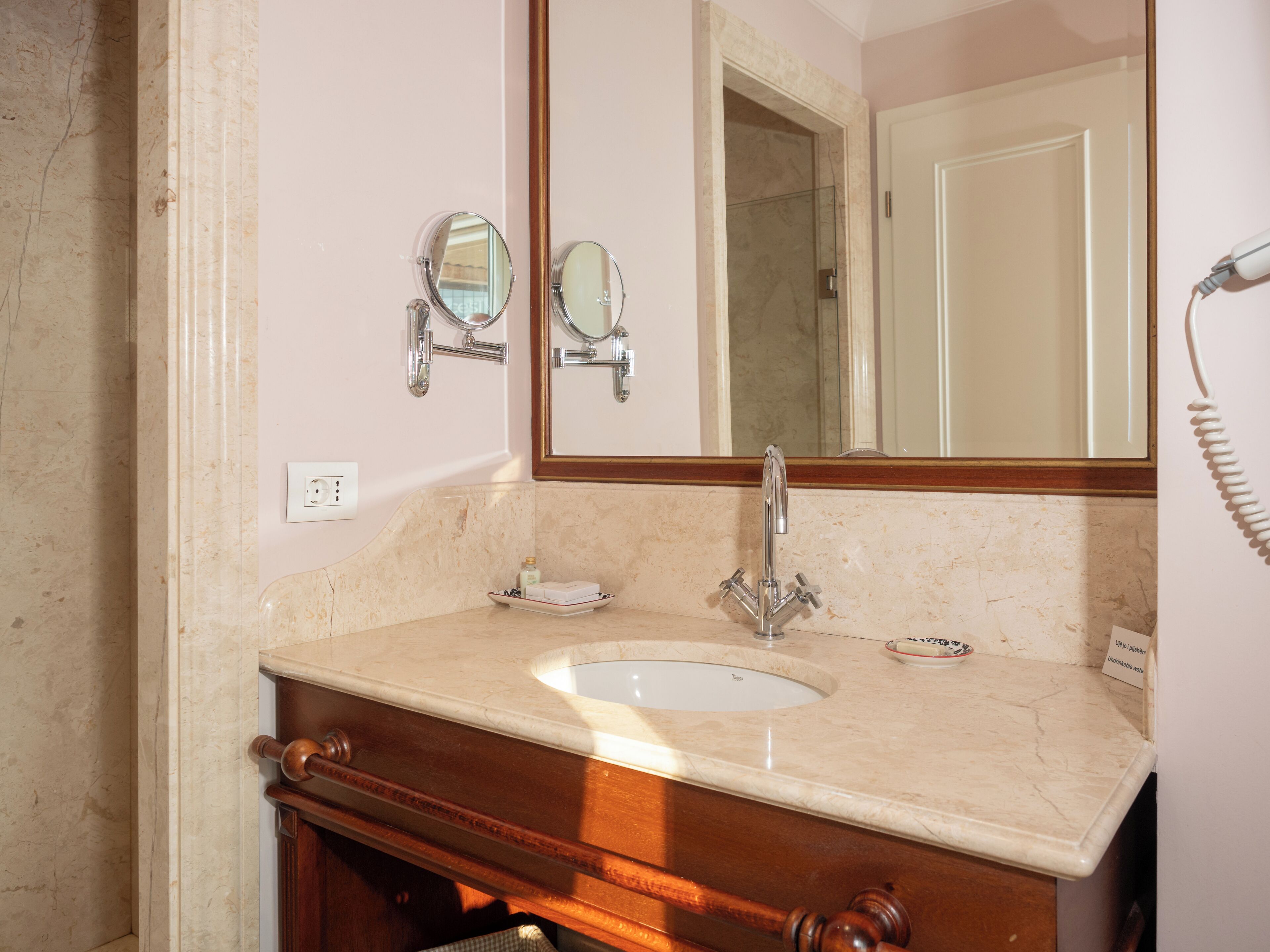 A bathroom with a sink, two mirrors, a towel rack, and a towel dispenser.