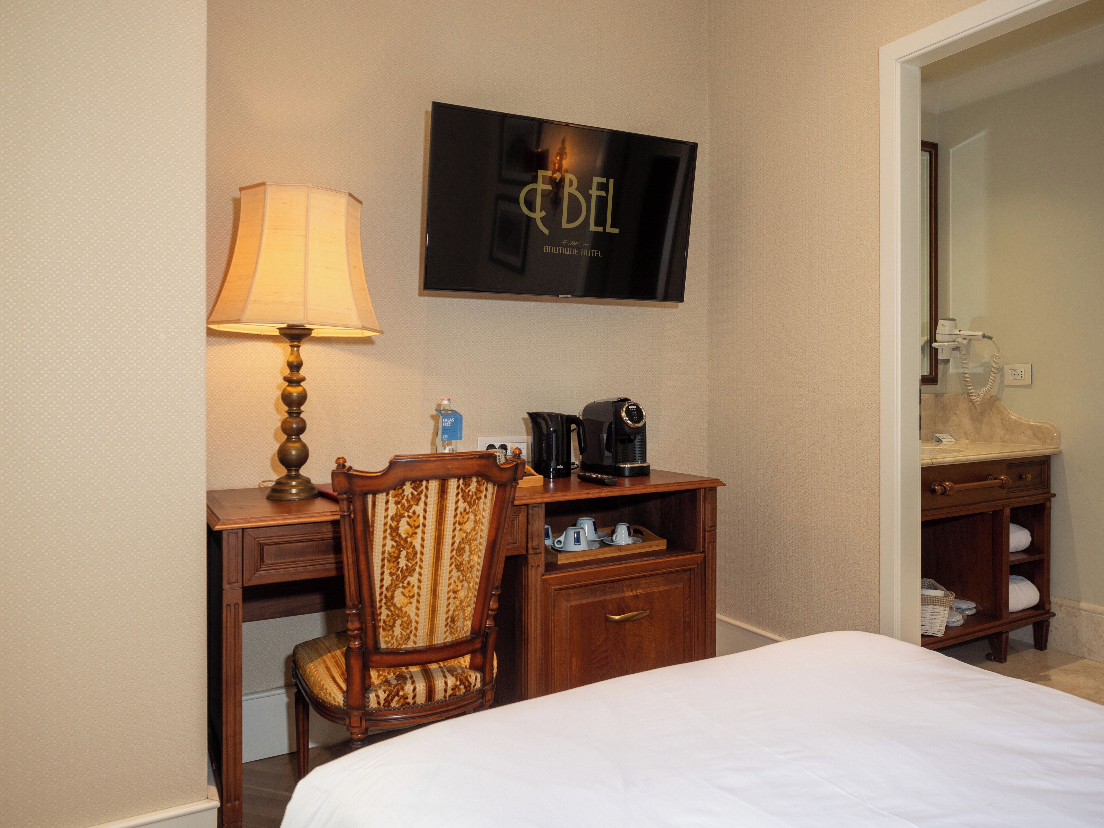 A hotel room with a bed, a desk with a lamp, a television, a coffee maker, and a bathroom mirror.