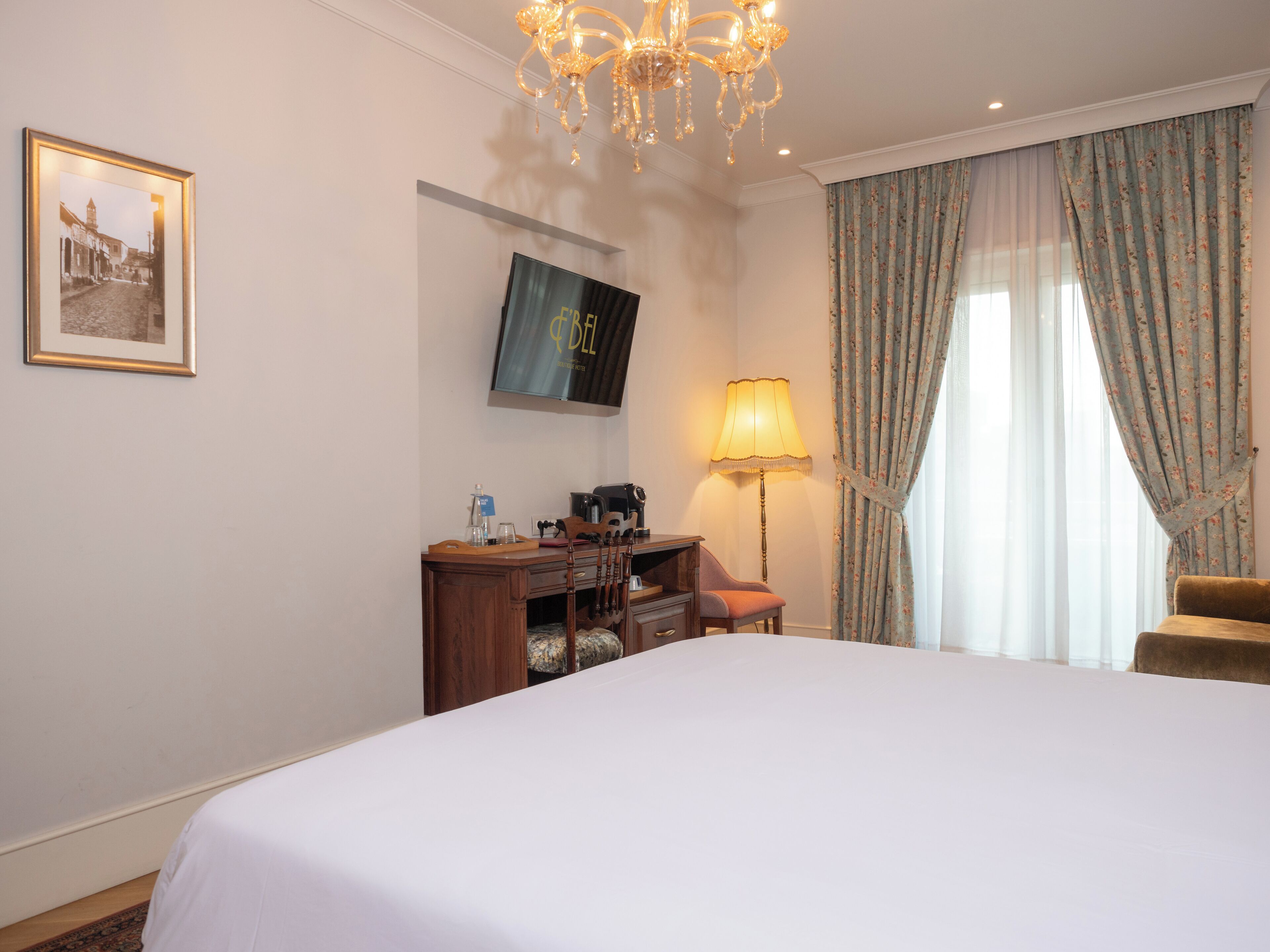 A hotel room with a bed, a desk with a computer, a television, a lamp, and curtains.