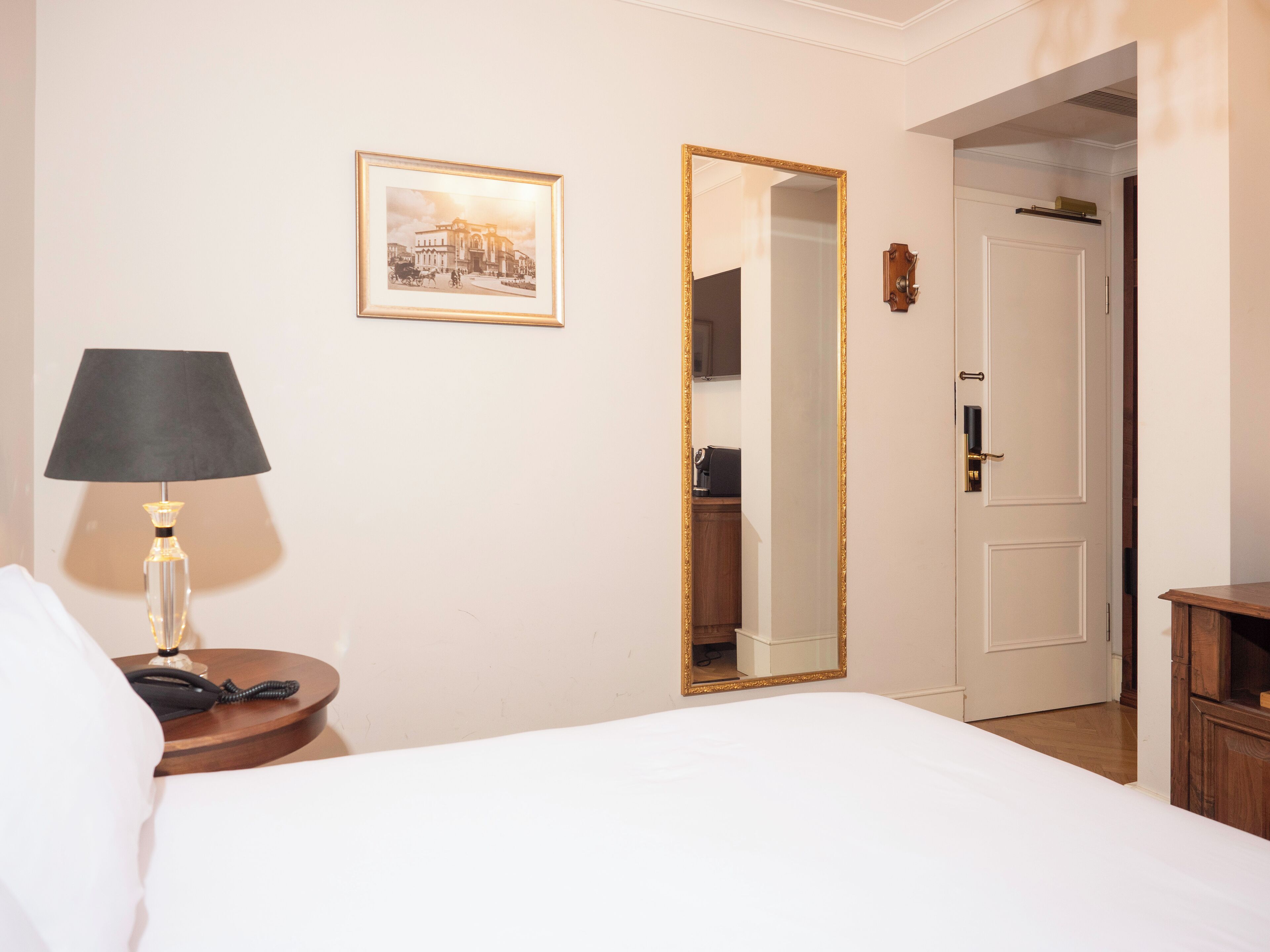 Una habitación de hotel con cama, lámpara de noche, un cuadro en la pared, un espejo y un armario.