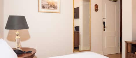 Una habitación de hotel con cama, lámpara de noche, un cuadro en la pared, un espejo y un armario.