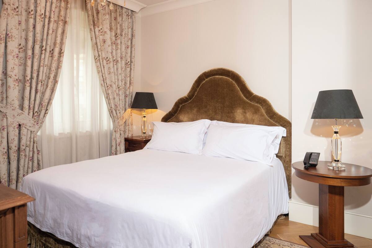 A neatly made bed with white linens, a wooden headboard, and a bedside table with a lamp and a phone.