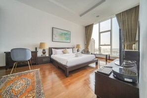 A hotel room with a large bed, two bedside tables with lamps, a desk with a computer, a TV, and a view of the city through large windows. - Waterfront Sea View Apt w/ Wow Factor on The Palm (Dubai)