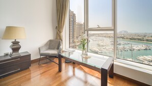 Une chambre moderne avec une table en verre, une chaise, une lampe et une vue sur une marina, visible à travers de grandes fenêtres.