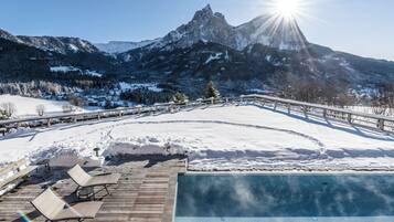 Un espacio al aire libre cubierto de nieve con una terraza de madera, sillones de descanso y una piscina.