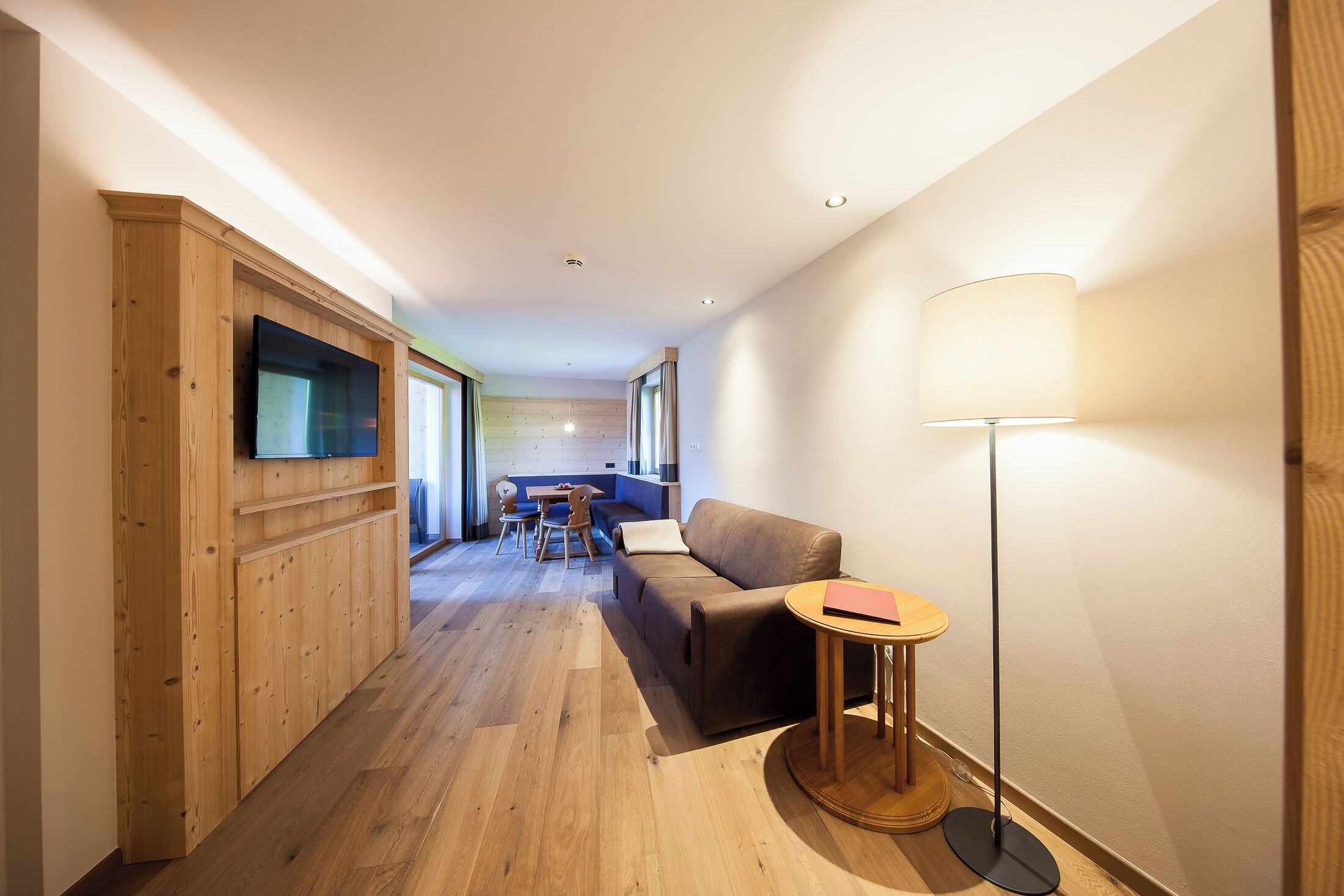A modern interior with a wooden floor, a sofa, a small round table, and a floor lamp.