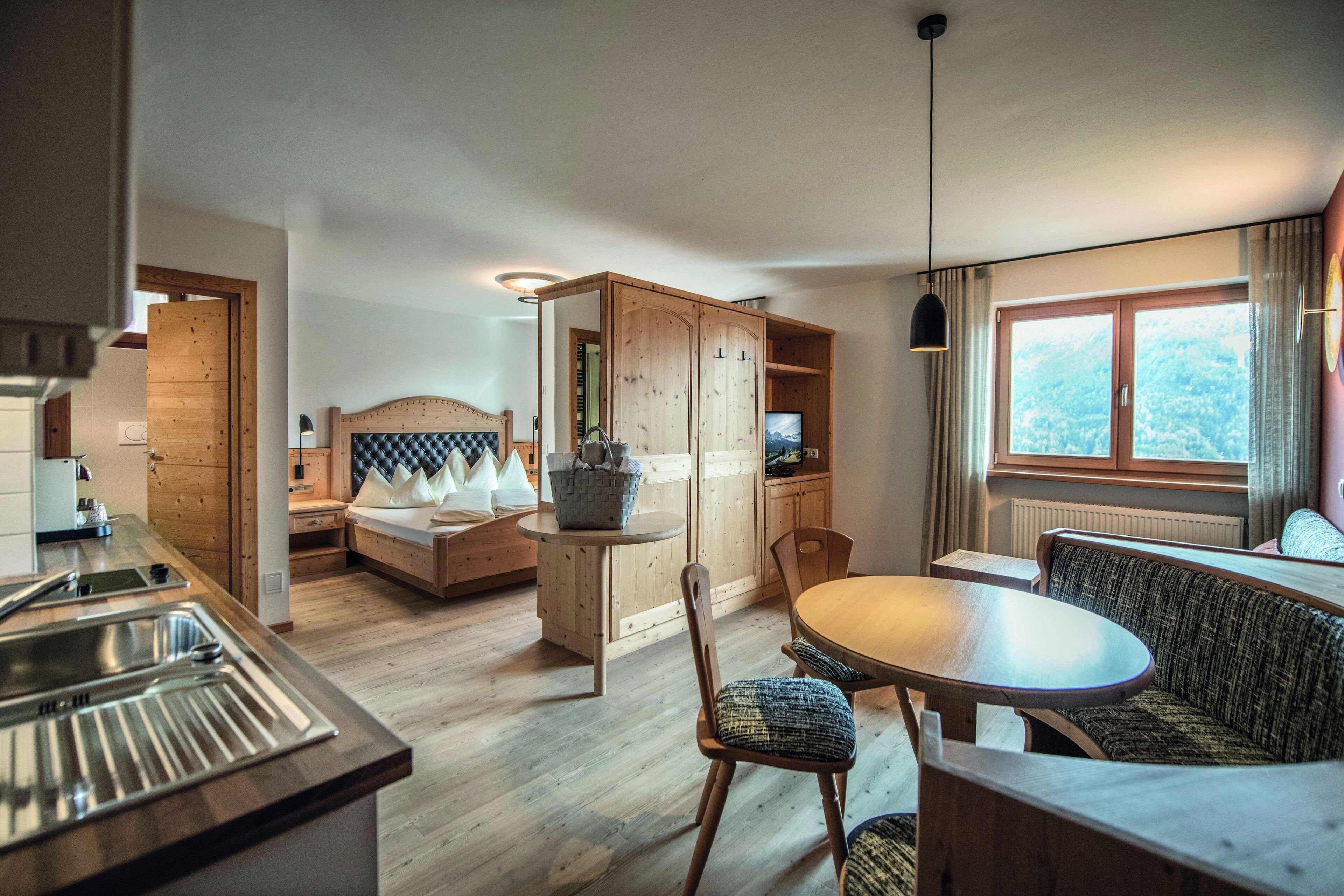 A modern kitchen with a wooden countertop and sink, a dining area with a round table and chairs, and a cozy seating area with a sofa and a cushioned bench.