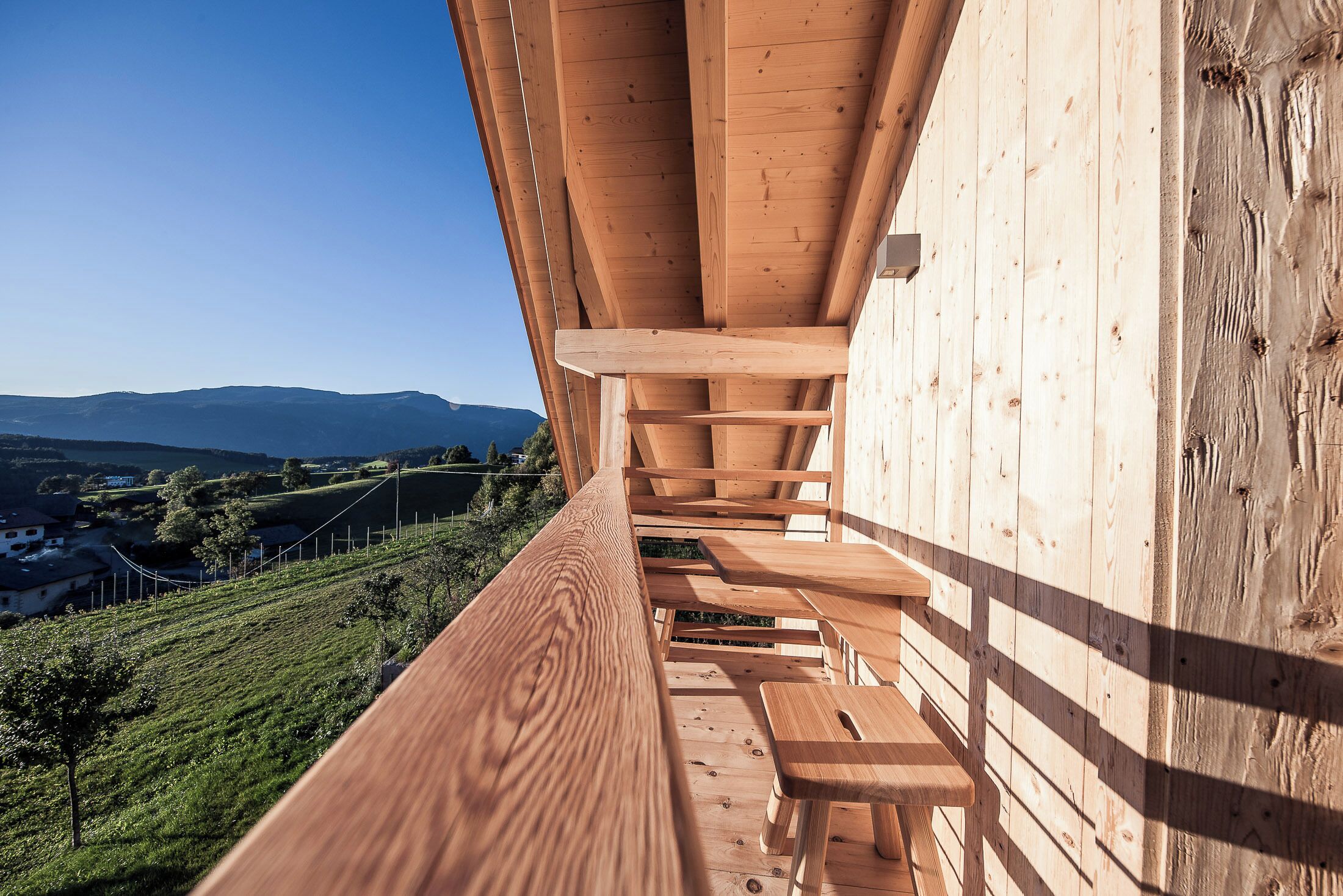 Une terrasse en bois avec des bancs, d’où l’on peut admirer un vignoble et des montagnes lointaines.