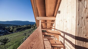 Une terrasse en bois avec des bancs, d’où l’on peut admirer un vignoble et des montagnes lointaines.