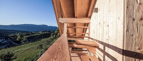 Une terrasse en bois avec des bancs, d’où l’on peut admirer un vignoble et des montagnes lointaines.