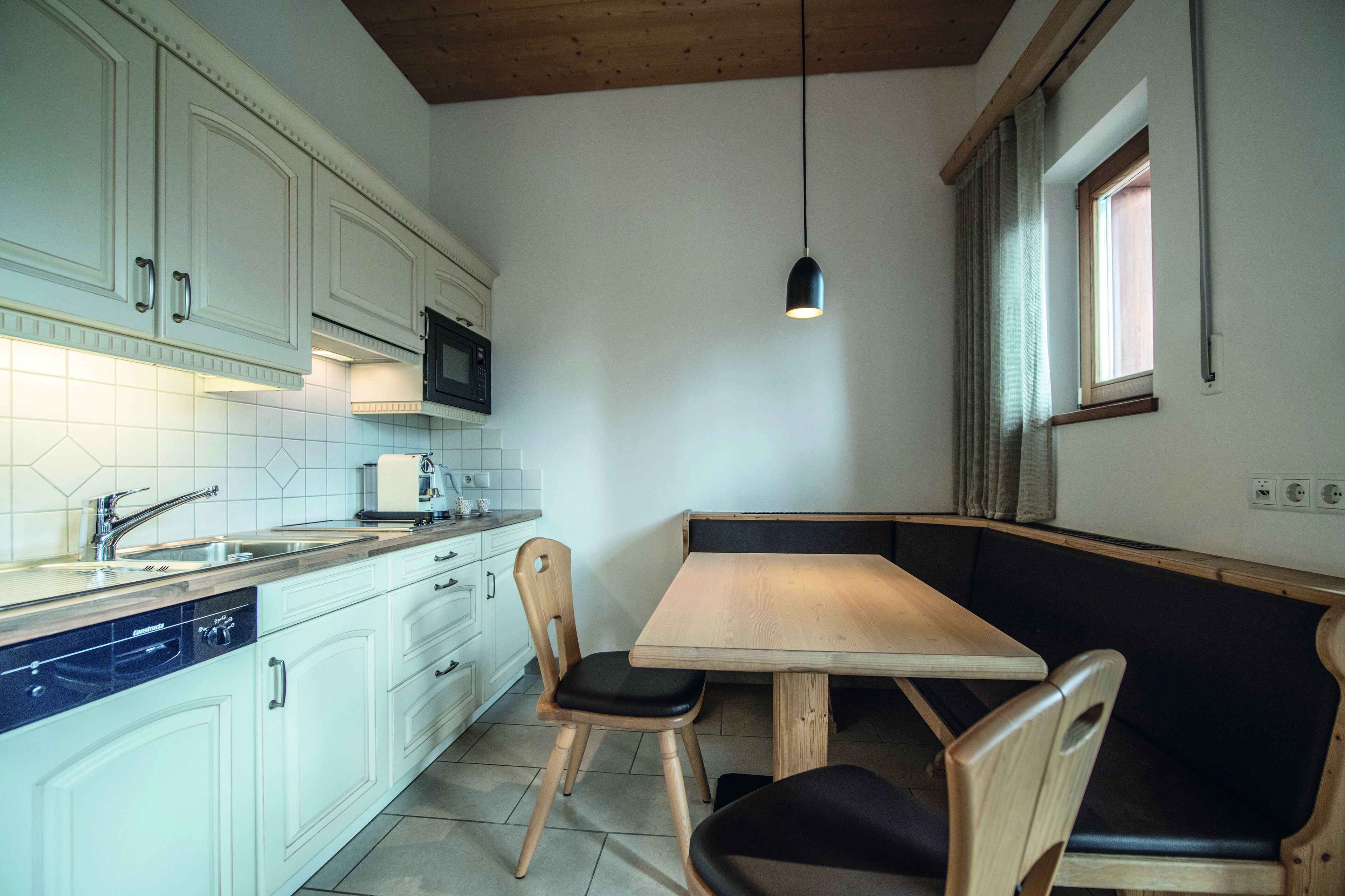 A compact kitchen with white cabinets, a wooden dining table, and a built-in bench.