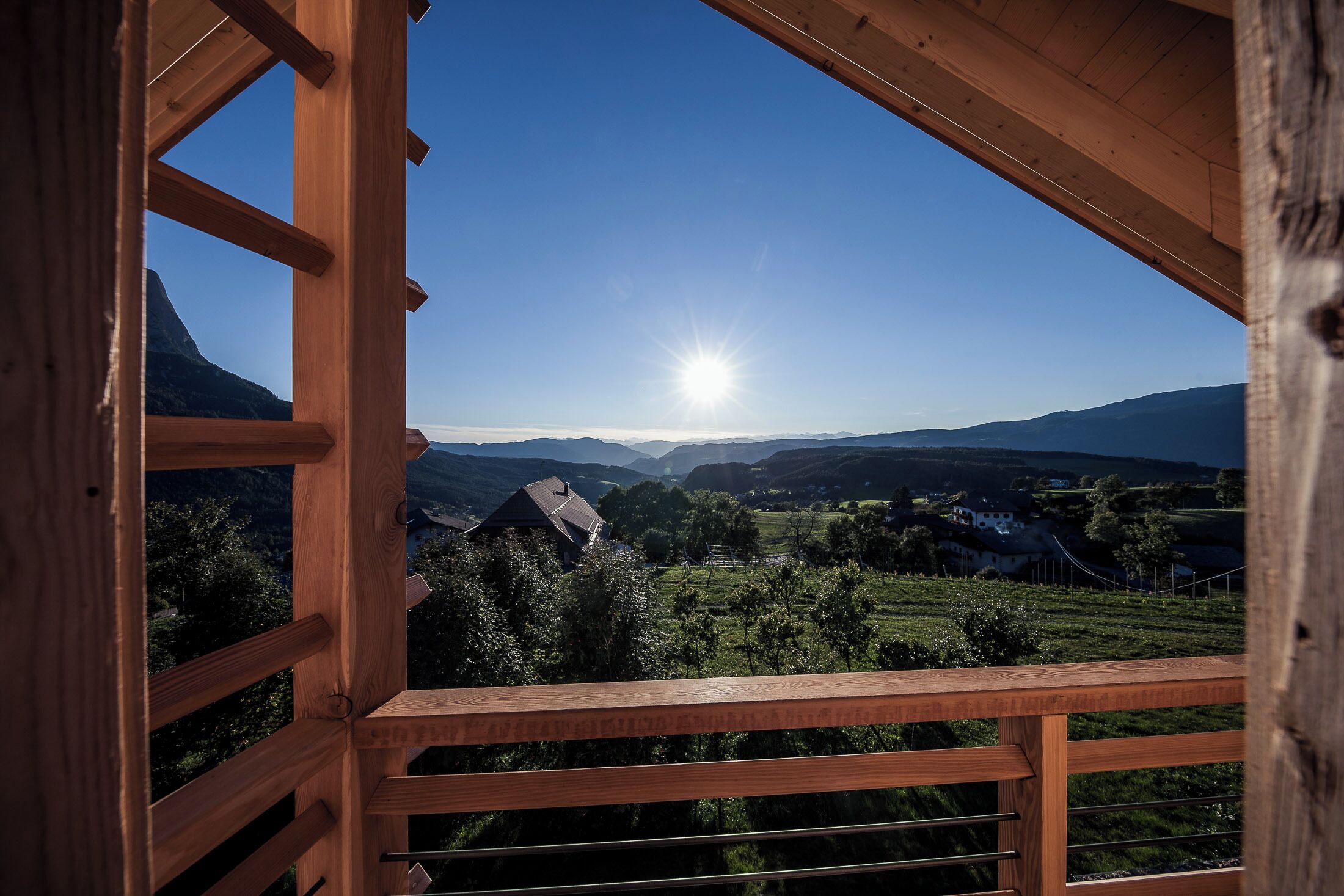 Un balcón de madera con vistas a un paisaje montañoso y un cielo despejado.