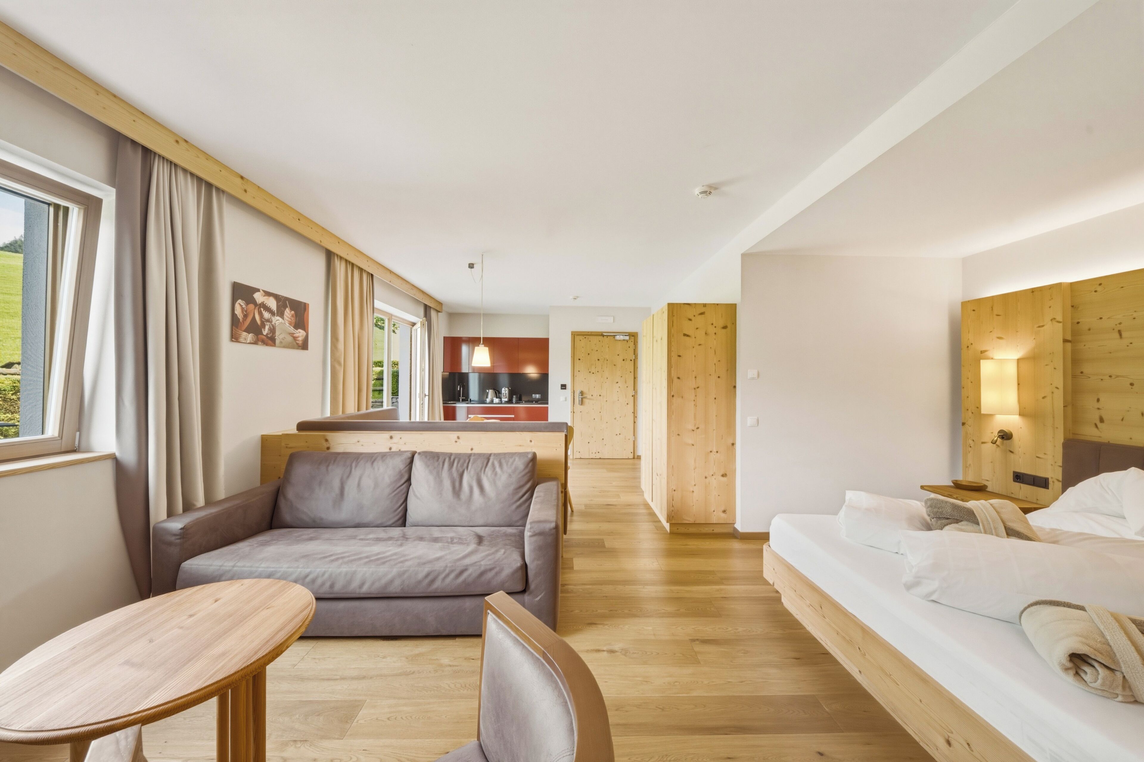 Une chambre d’hôtel moderne avec un canapé, une table à manger, un lit et un coin cuisine à l’arrière-plan.