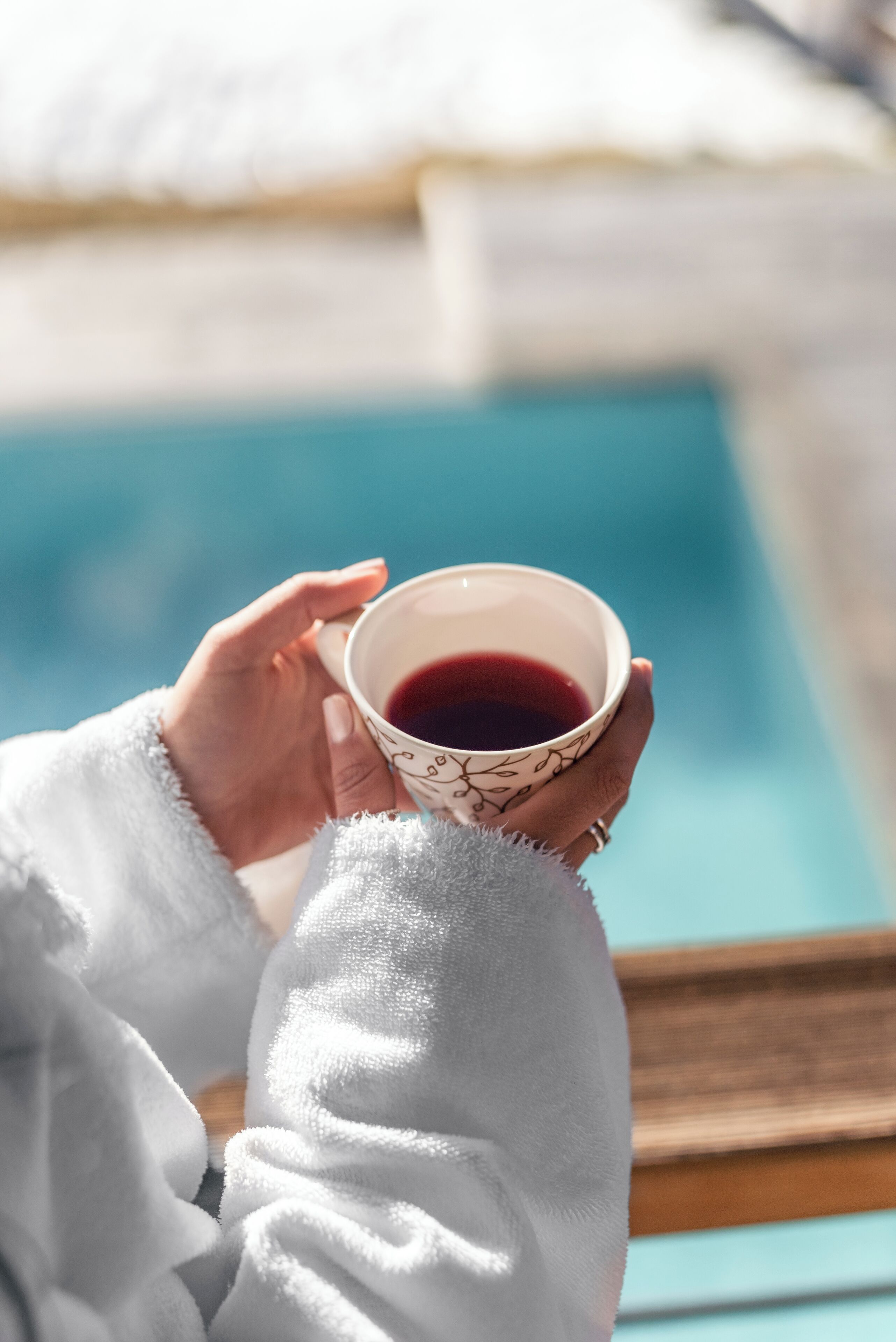 A person holding a cup of tea by a poolside.