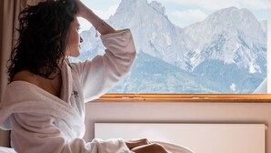 A person sitting on a bed with a mountain view through a window. - Sonus Alpis - Adults Only (Castelrotto)