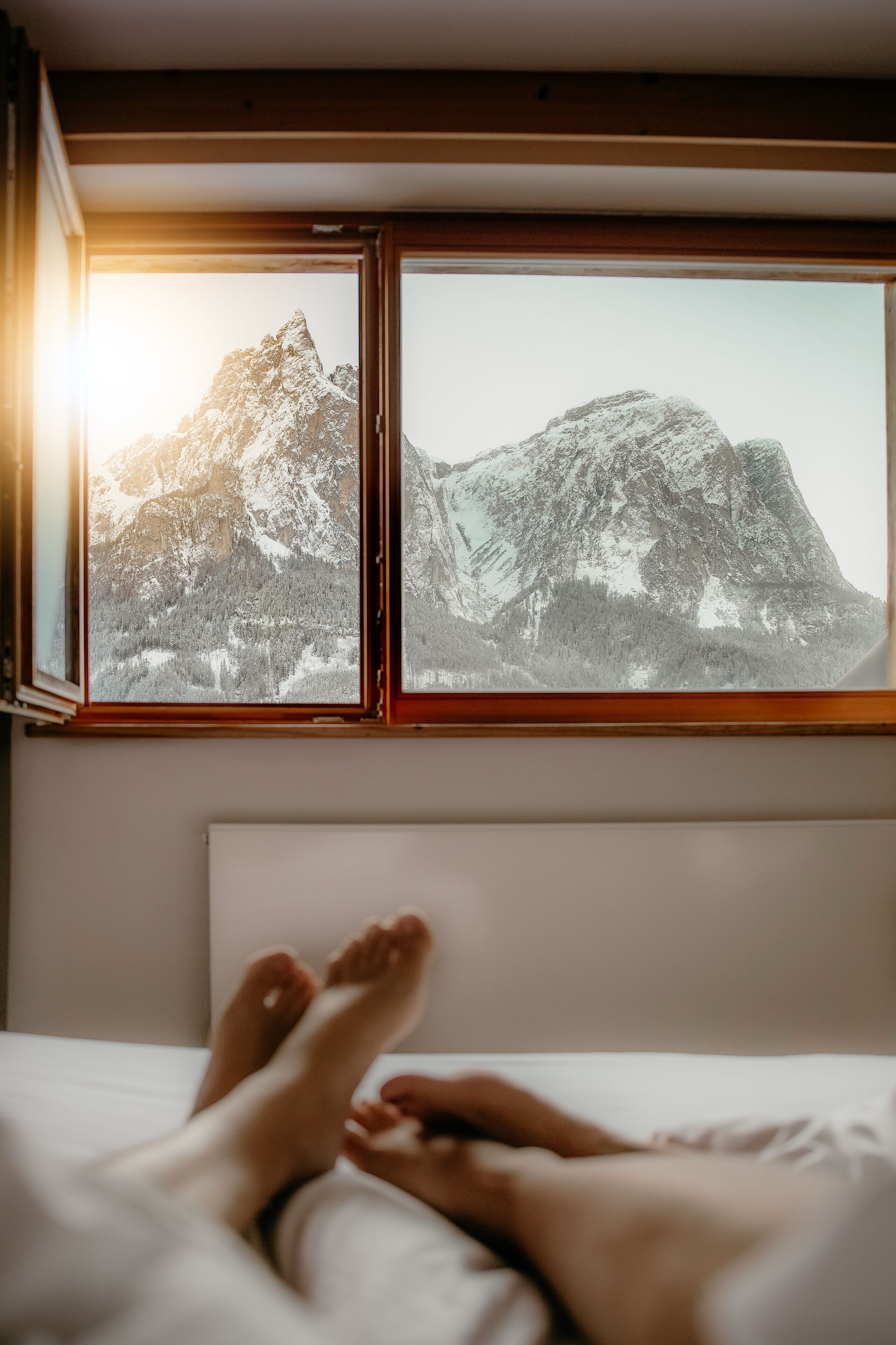 A bed with a view of a mountain through a window.