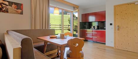 Uma sala de estar moderna com um banco de madeira, uma mesa de jantar e uma cozinha ao fundo.