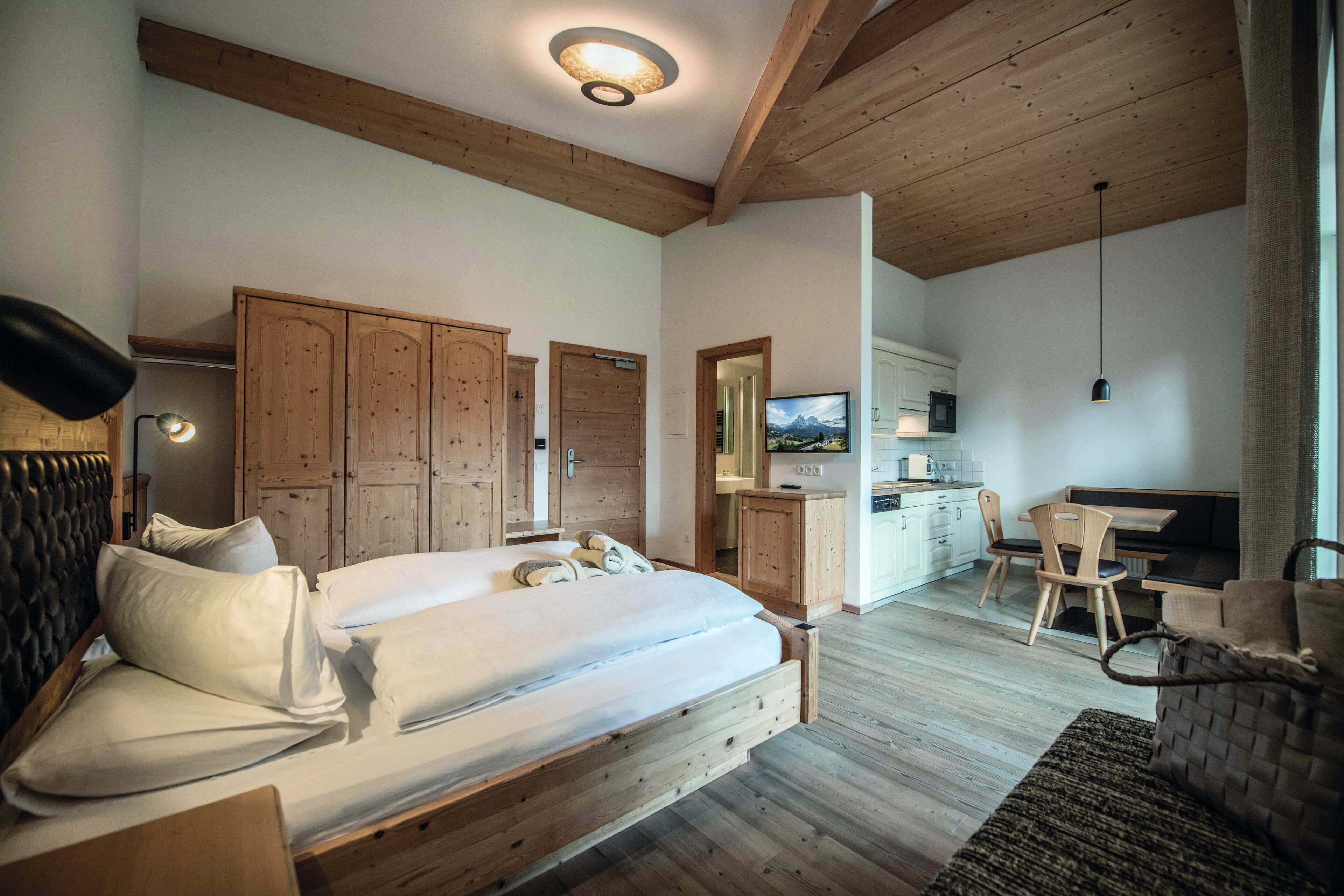 A bedroom with a wooden bed, a desk, a chair, and a kitchenette.