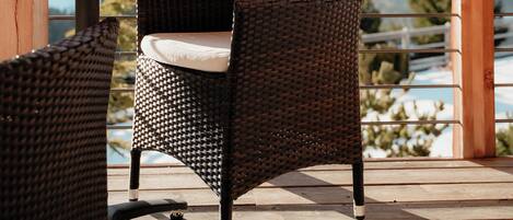 A wooden deck with wicker chairs and a table, overlooking a mountainous landscape.