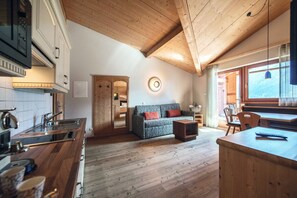 Ein geräumiger Wohnbereich mit Holzbalkendecke, einer Couch, einem Couchtisch und einer Küche mit modernen Geräten.