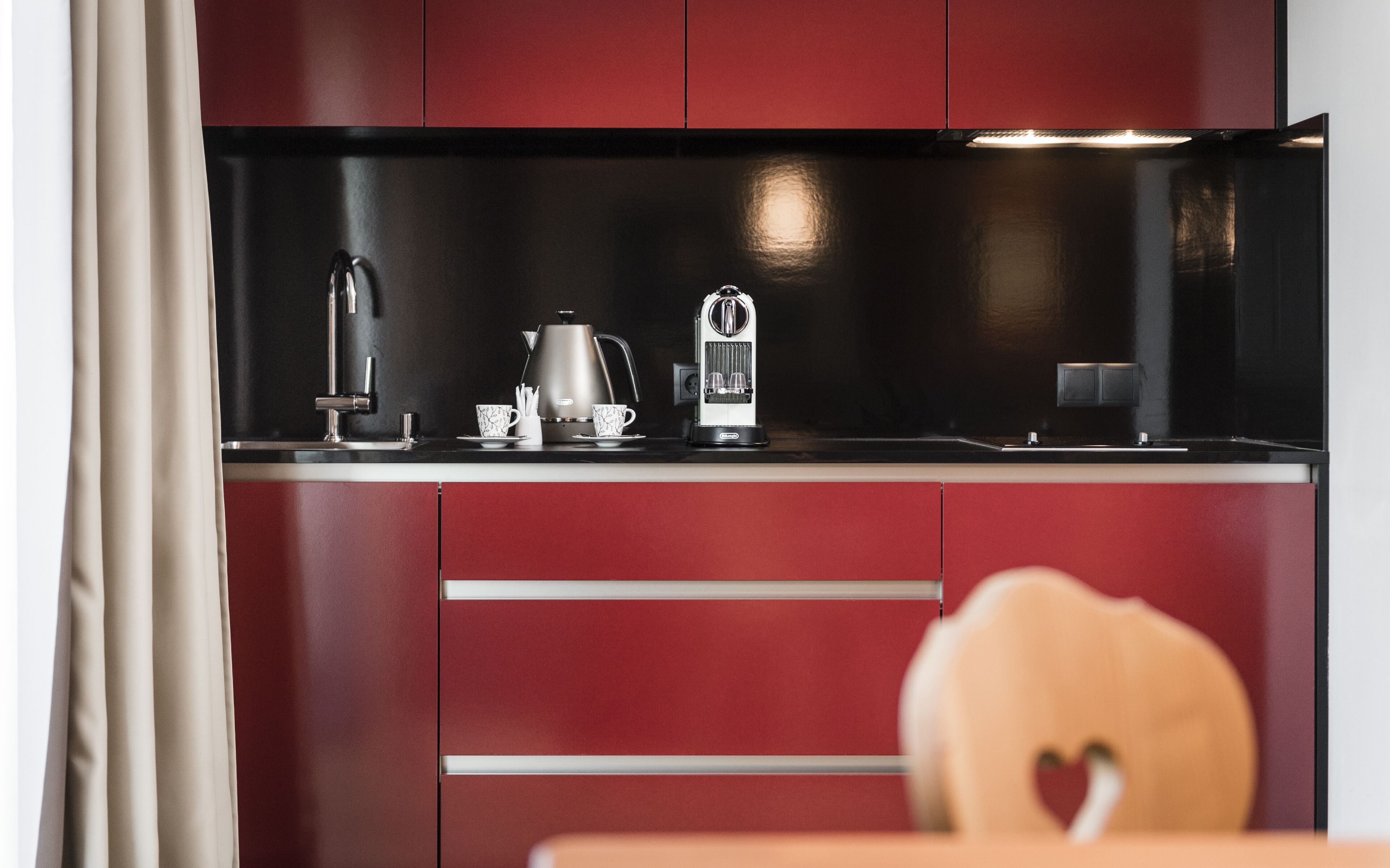A modern kitchen with a black countertop, stainless steel appliances, and red cabinetry.